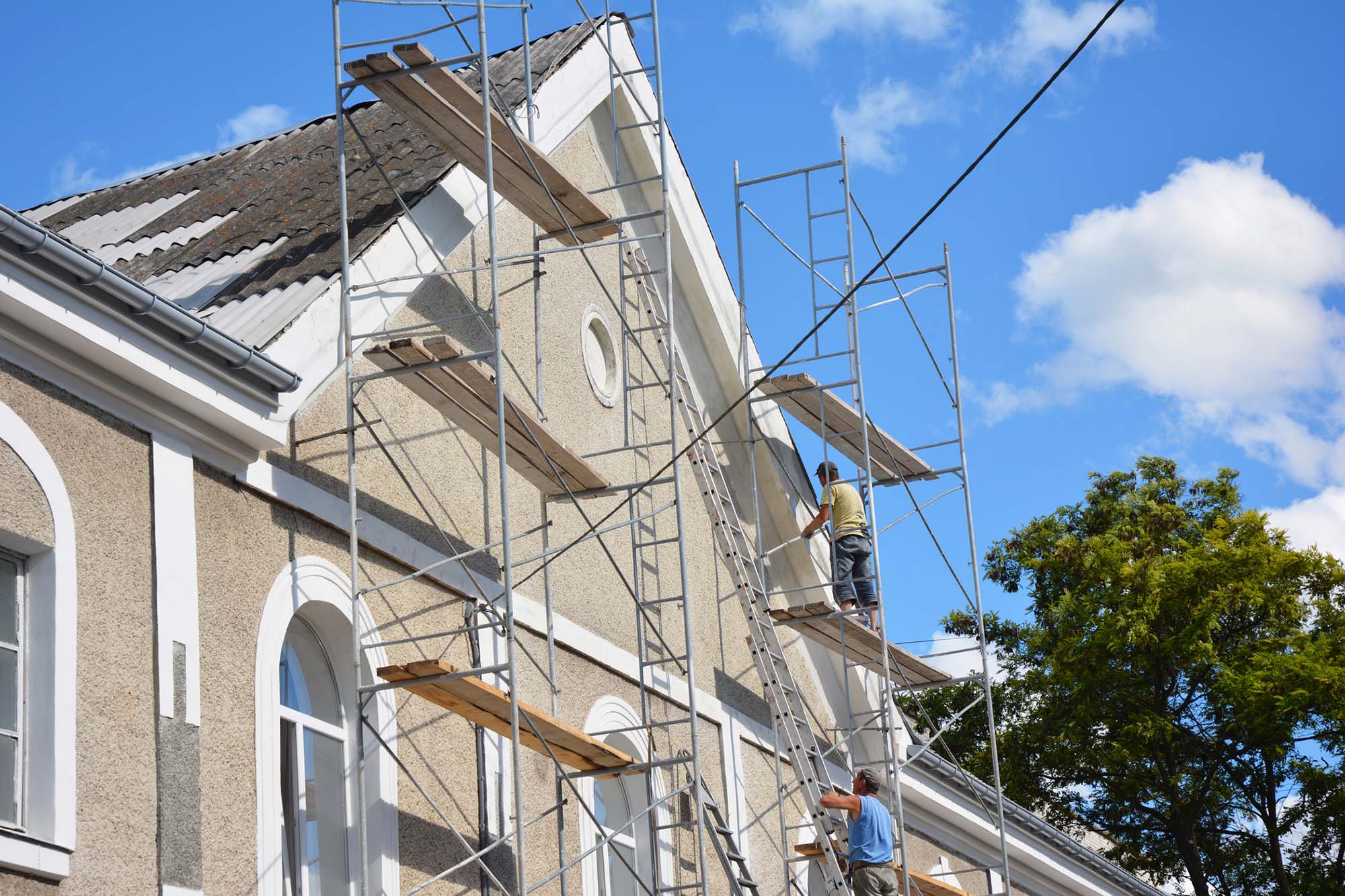 KYIV, UKRAINE - December, 27, 2018: Contractors plastering house facade outdoor. Painting and plastering exterior house scaffolding wall with asbestos roof repair